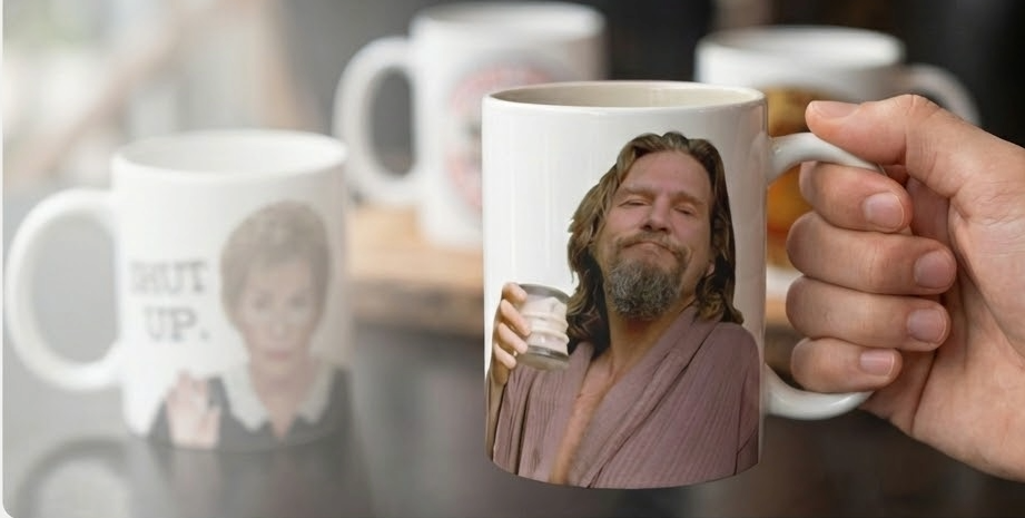 Person holding a mug with a printed image of a The Dude, with other mugs in the background.